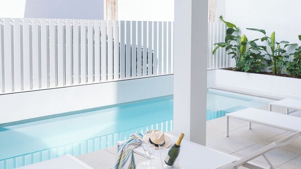 A poolside area with white lounge chairs, a table with a bottle of champagne, and a tiled floor. - Two-bedroom apartment (Picaña)