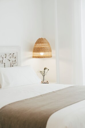 A bed with a white headboard, a woven lamp, and a vase with dried flowers.