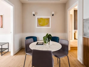 Uma sala de jantar moderna com uma mesa redonda de mármore, quatro cadeiras cinzas, uma planta em vaso e duas obras de arte emolduradas na parede.