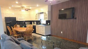 A modern living room with a glass coffee table, grey sofas, and a dining area with wooden chairs and a table. - Chelsea Chalet - 4BR, Comfortable Stay Near It All (Atlantic City)