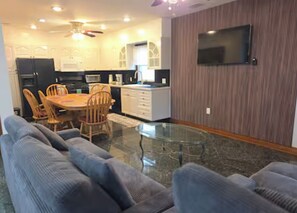 A modern living room with a glass coffee table, grey sofas, and a dining area with wooden chairs and a table. - Chelsea Chalet - 4BR, Comfortable Stay Near It All (Atlantic City)