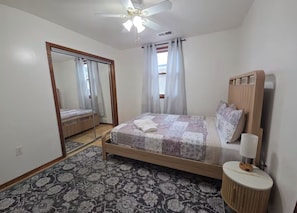 A bedroom with a bed, a mirror, a ceiling fan, a bedside table with a lamp, and a patterned rug. - Chelsea Chalet - 4BR, Comfortable Stay Near It All (Atlantic City)