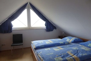 Een slaapkamer met een enkel bed, een stoel, een bureau en een raam met gordijnen.