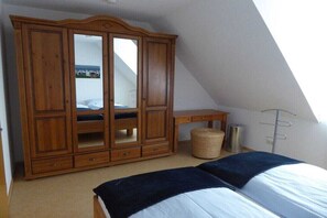 A bedroom with a bed, a wooden wardrobe, a small desk, and a window. - Holiday home with 3 bedrooms (Norddeich)