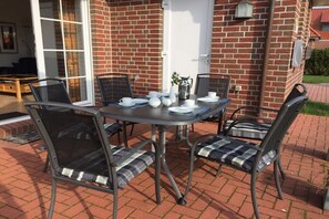 A patio with a table set for four, surrounded by chairs with cushioned seats. - Holiday home with 3 bedrooms (Norddeich)