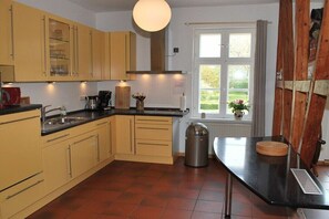 A kitchen with cabinets, a sink, a stove, a window with curtains, and a trash can. - One-bedroom apartment (Sagard \/ Neddesitz)