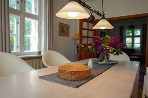 A dining area with a table, chairs, a woven centerpiece, a vase with flowers, and pendant lighting. - One-bedroom apartment (Sagard \/ Neddesitz)