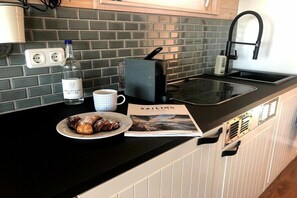 Un comptoir de cuisine avec une machine à café, une bouteille d’eau, une tasse, une assiette avec de la nourriture et un magazine.
