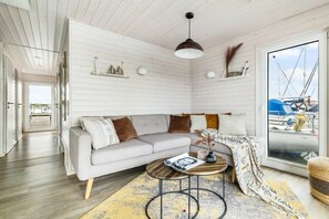 Un salon moderne avec un canapé, une table basse et une vue sur les bateaux, visible à travers une grande fenêtre.