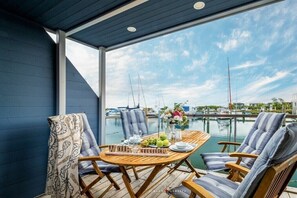 A covered outdoor seating area with a table set for two, overlooking a marina with boats. - Holiday home in Kragenaes with terrace (Kragenaes)
