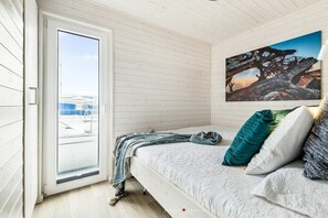 Een slaapkamer met een bed, kussens, een deken, een raam en een schilderij aan de muur.