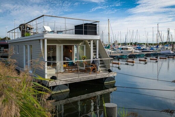 Una casa flotante con terraza, ventanas y una escalera que lleva al nivel superior.