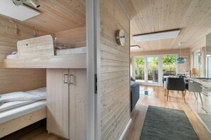 Un interior moderno con paredes de madera, una litera, una zona de comedor y ventanas amplias.