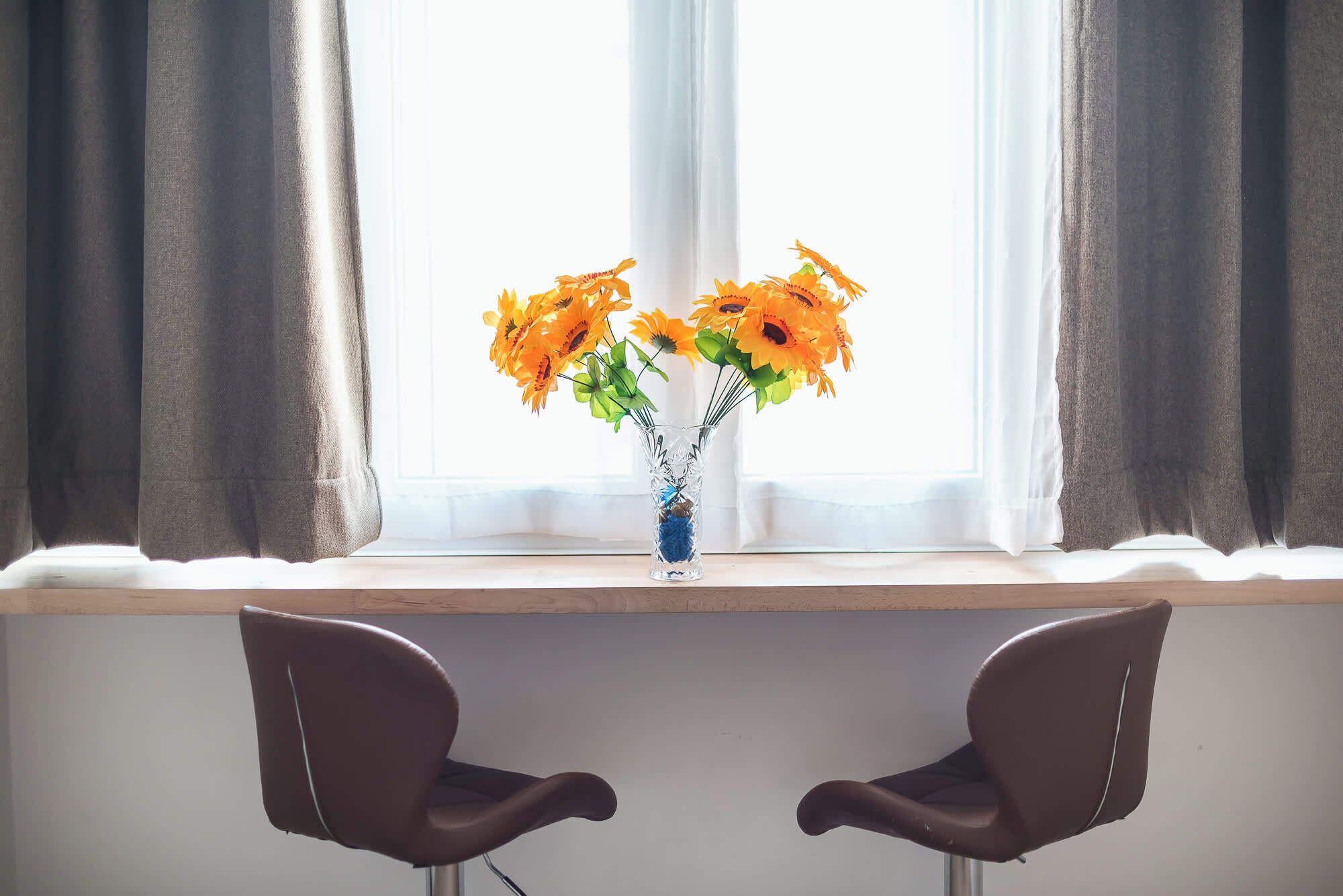 A window with a vase of orange flowers, two brown chairs, and a white window frame.