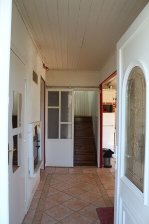 Ein Korridor mit Holzboden, gefliestem Fußboden, einer weißen Tür mit Glasfeldern und einer Treppe, die in einen Küchenbereich führt.