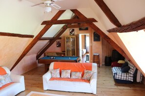 Ein Loft-Zimmer mit Poolbillard, zwei Sofas, Holzbalken und Deckenventilator.