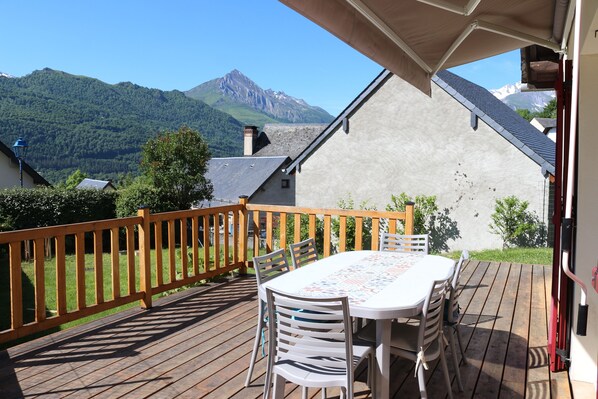 Eine Holzterrasse mit Tisch und Stühlen, mit Blick auf eine gebirgige Landschaft.
