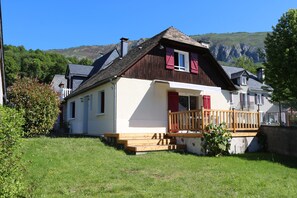 Ein zweistöckiges Haus mit einer Holzterrasse, einer kleinen Veranda und einem Berg im Hintergrund.
