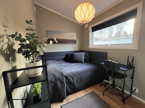 Een slaapkamer met een bed, nachtkastje, lamp, kamerplant en een raam met uitzicht.
