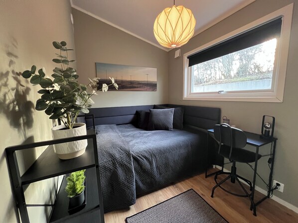 Un dormitorio con cama, mesita de noche, lámpara, planta en maceta y ventana con vistas.