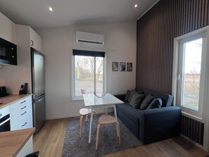 Una cocina moderna con refrigerador empotrado, una mesa de comedor con sillas, un sofá azul oscuro y un amplio ventanal con vistas al exterior.