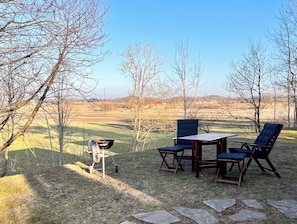 Een terras met een tafel en stoelen, omringd door bomen en uitzicht op een veld.