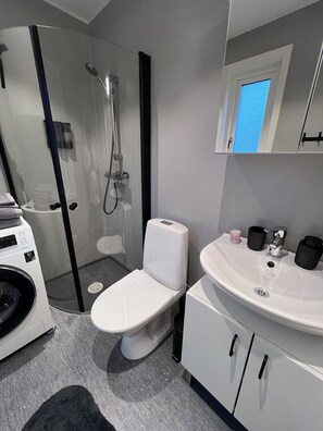 Un baño moderno con ducha de vidrio, inodoro blanco, lavamanos con tazas negras y lavadora.