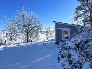 A snow-covered landscape with a small cabin and bare trees.