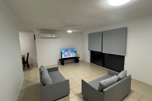 Ein Wohnzimmer mit Flachbildfernseher, grauen Sofas, Deckenventilator und Fliesenboden.
