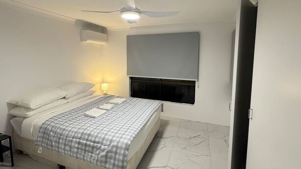 A bedroom with a bed, a ceiling fan, a wall-mounted TV, and a fireplace. - Family-friendly home—feel right at home. (Crestmead)