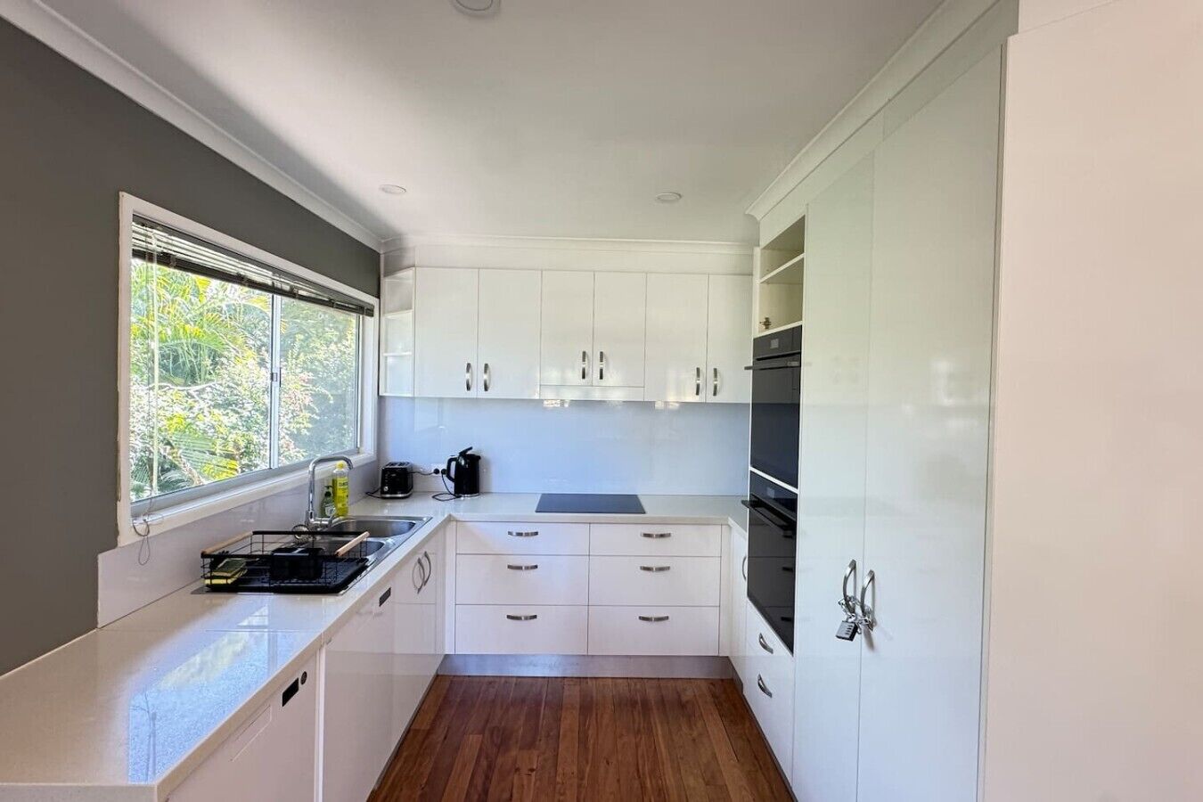 A compact kitchen with white cabinetry, a window, and a built-in oven.