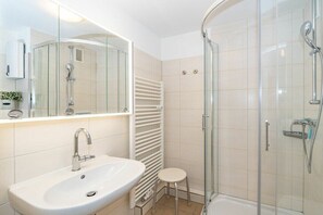 Uma casa de banho moderna com chuveiro de vidro, lavatório branco e suporte para toalhas.