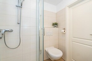 Une salle de bain avec une douche à parois de verre, des toilettes et une petite plante en pot accrochée au mur.