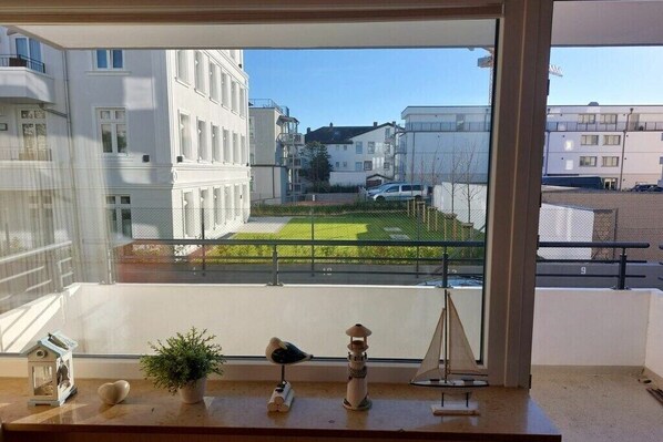 Varanda com vista para uma área residencial, um pequeno vaso com planta, uma estatueta de pássaro e um sino de vento decorativo.