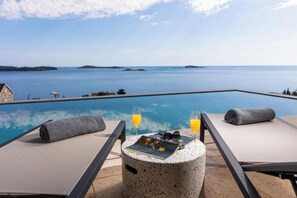 Area relax a bordo piscina con vista sul mare, un tavolino con bevande e poltrone prendisole.