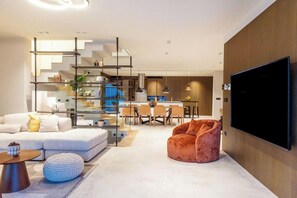 Un salon moderne avec un canapé, un pouf et un téléviseur.