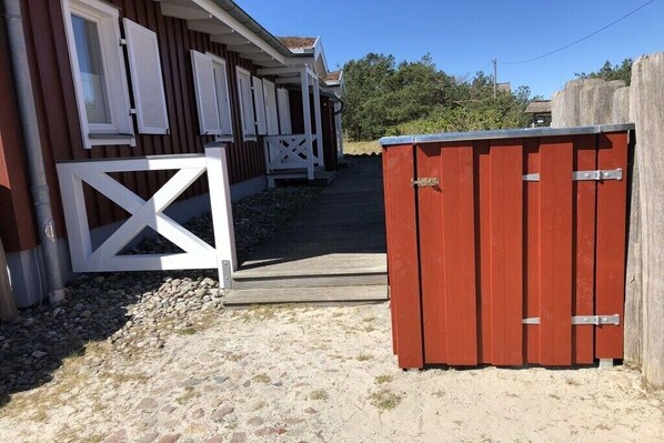 A wooden deck leading to a building with white-framed windows and a red storage shed. - Prerow || beach house (Prerow)