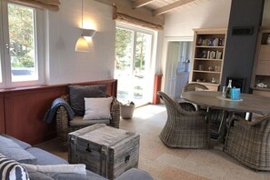 Een gezellige zithoek met een bank, rieten stoelen, een houten salontafel en een boekenkast.