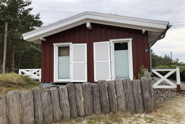 A small, single-story wooden building with two windows and a white door, surrounded by a wooden fence. - Prerow || beach house (Prerow)