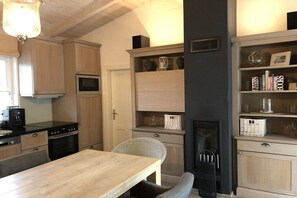 A kitchen with wooden cabinets, a microwave, a dining table with chairs, a fireplace, and a bookshelf. - Prerow || beach house (Prerow)