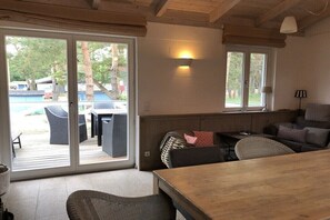 A room with a wooden table, wicker chairs, a sofa, and a sliding glass door leading to an outdoor area with a pool. - Prerow || beach house (Prerow)