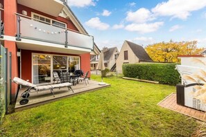 Una casa de dos pisos con un balcón, un jardín y un patio con mesa y sillas.