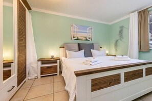 Un dormitorio con una cama, mesitas de noche, un velador, una ventana con cortinas y un cuadro colgado en la pared.