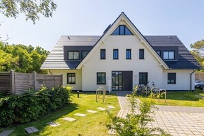 Moderni, kaksikerroksinen talo, jossa on kalteva katto, pääsisäänkäynti ja pieni etupiha, josta polku johtaa ovelle.