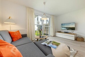 A modern living room with a sofa, a lamp, a TV, and a window with curtains. - One-bedroom apartment (Ostseebad Zingst a Darß)