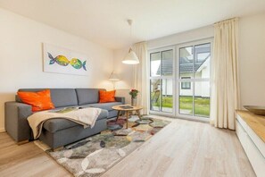 A modern living room with a sofa, a coffee table, a painting, and a large window. - One-bedroom apartment (Ostseebad Zingst a Darß)