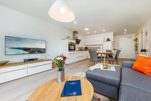 A modern living room with a sofa, a coffee table, a TV, and a dining area with chairs and a table. - One-bedroom apartment (Ostseebad Zingst a Darß)
