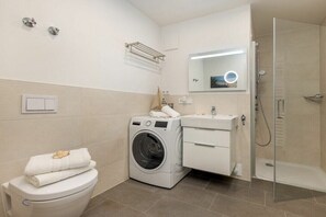 A modern bathroom with a washing machine, toilet, sink, and shower. - One-bedroom apartment (Ostseebad Zingst a Darß)