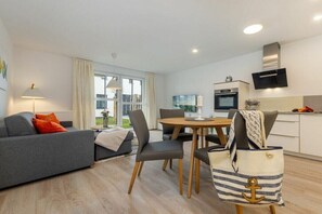 A modern living room with a sofa, dining table, chairs, and a kitchen area with a microwave and oven. - One-bedroom apartment (Ostseebad Zingst a Darß)