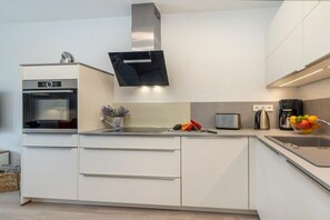 A modern kitchen with a built-in oven, a stainless steel range hood, a coffee maker, and a fruit bowl. - One-bedroom apartment (Ostseebad Zingst a Darß)